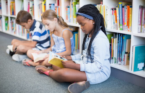 Image shows three students on floor in school library reading.