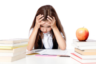 Image shows frustrated little girl reading with stack of books around her.