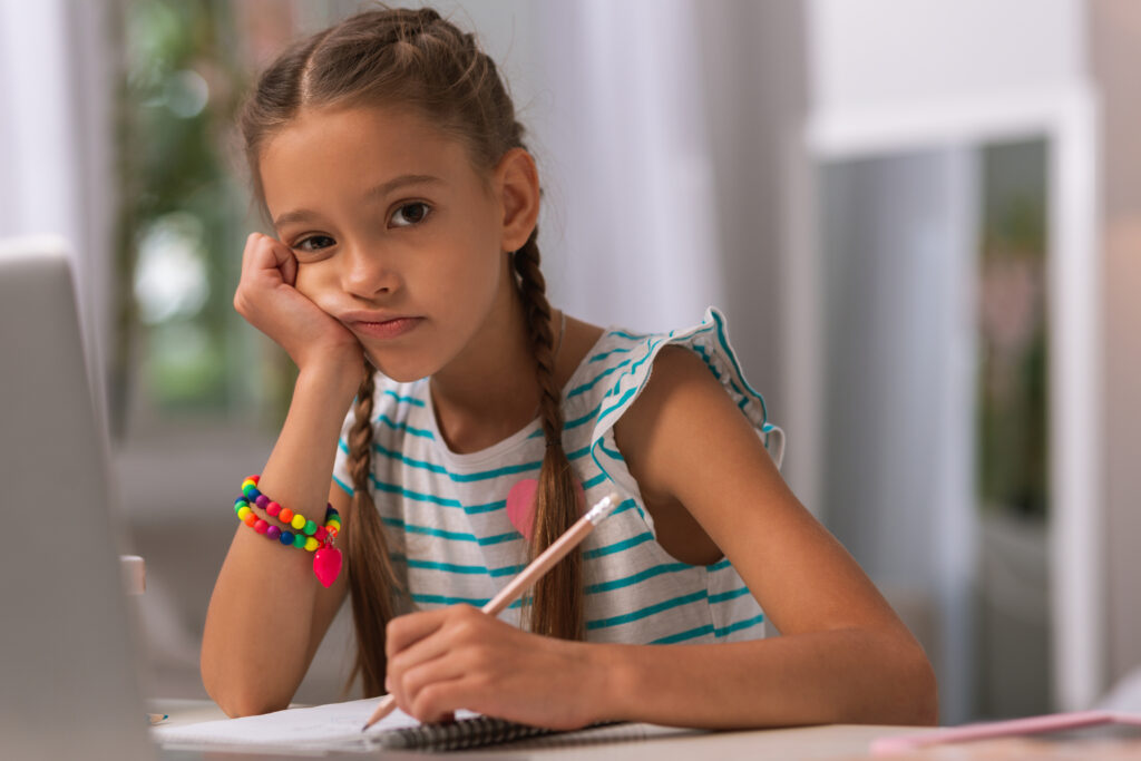 Young girl with chin in hand holding pencil looking frustrated with writing.