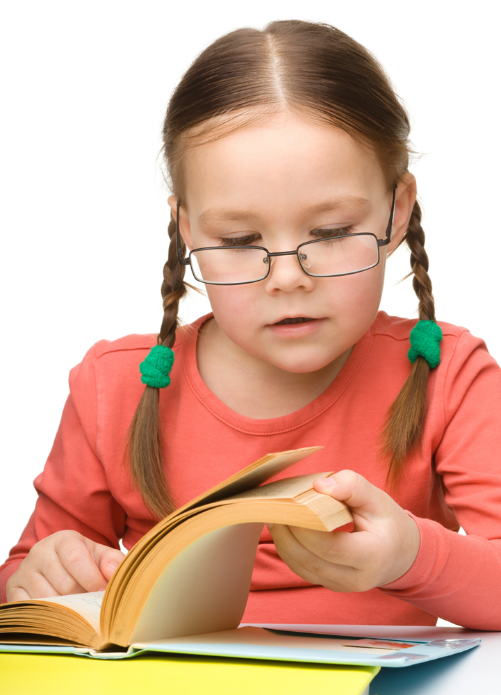 Little girl with braided hair in orange shirt making meaning of her reading.
