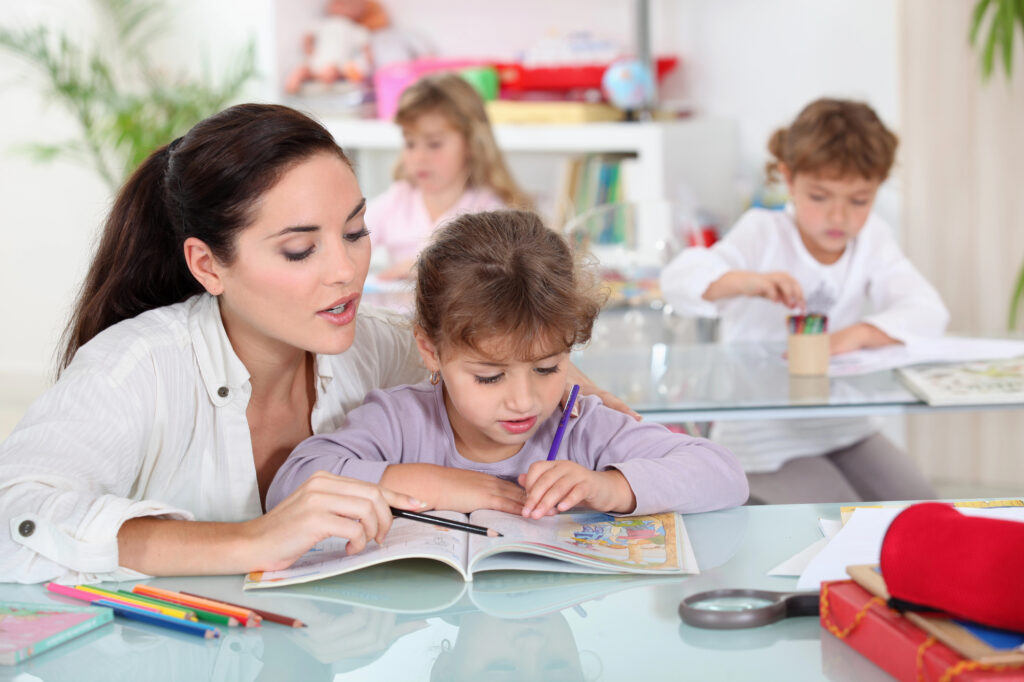 Teacher with brown hair and white listening to child with purple shirt read a book to conduct an informal reading assessment.