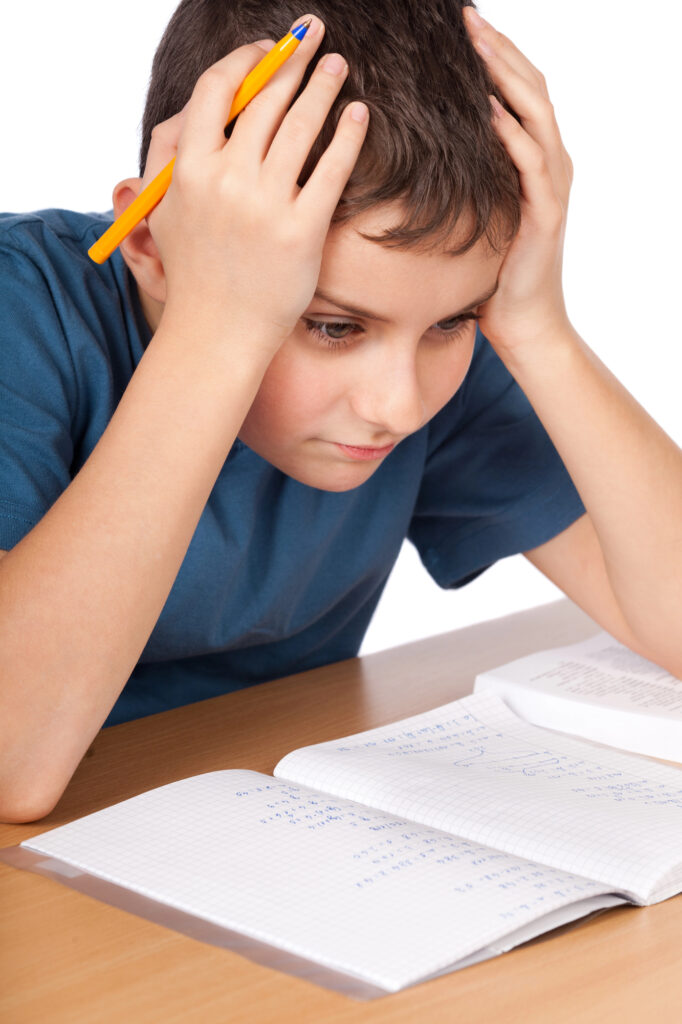Confused boy with hands on head and pencil in hand with notepad on table