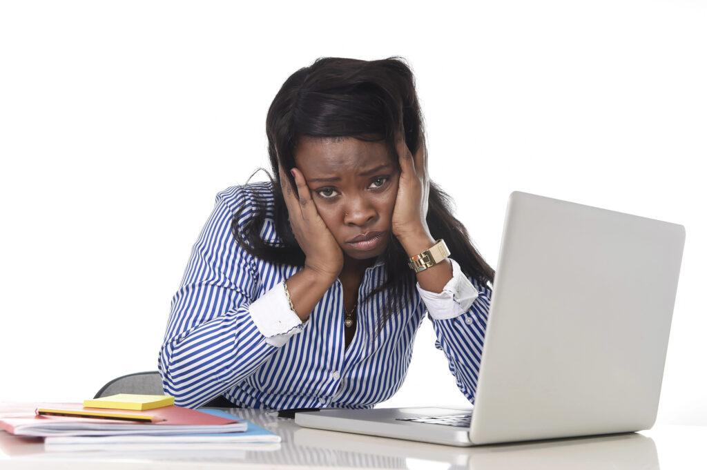 Frustrated teacher in striped shirt in front of computer with stack of notebooks.  