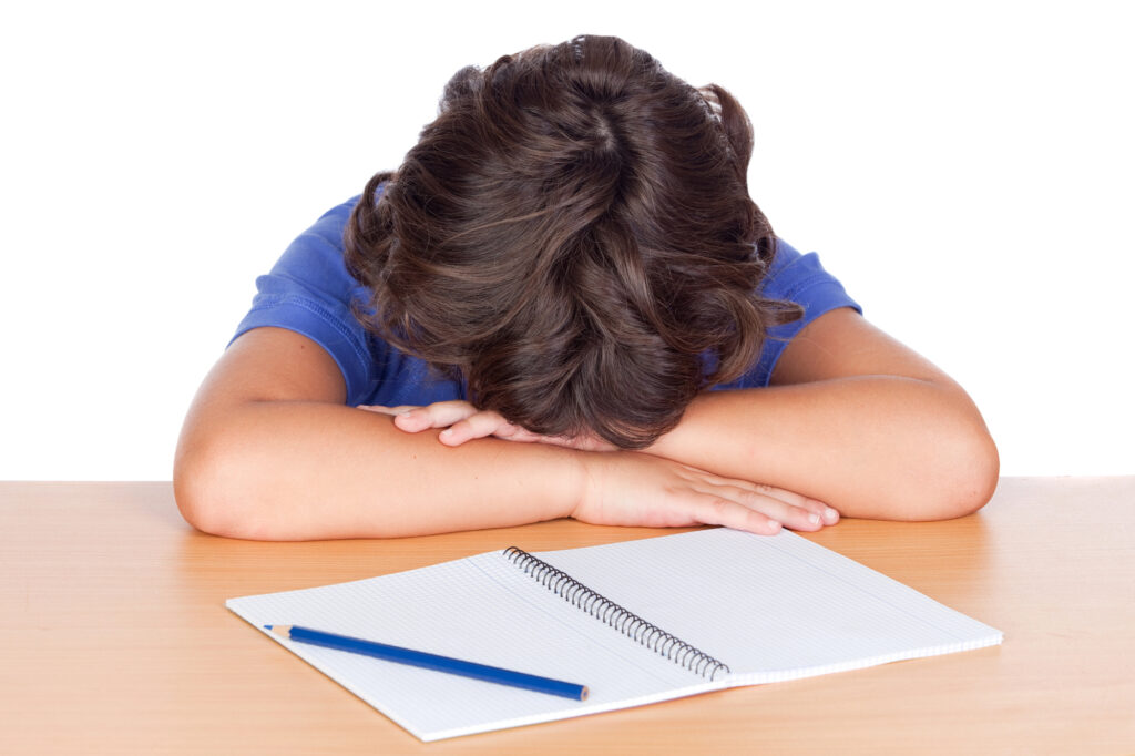 Frustrated student with head down and blank notebook page with blue pencil.