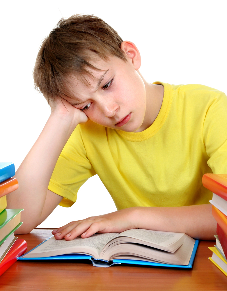 Boy in yellow shirt with head on hand bored with reading a book.