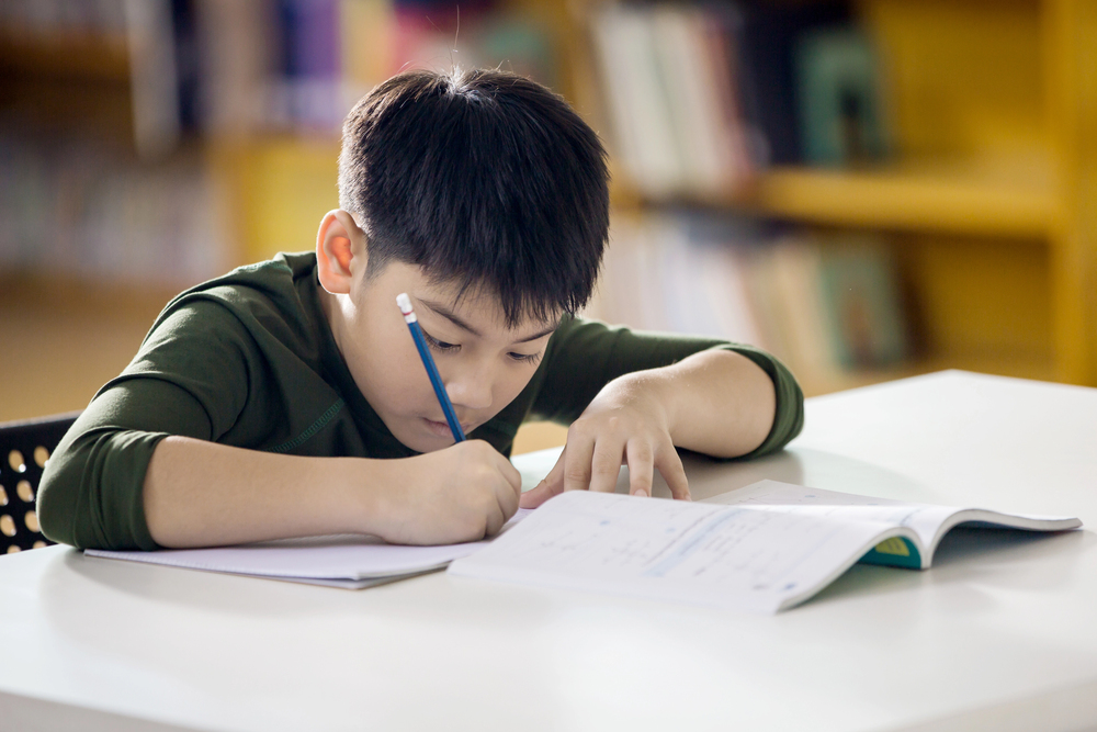 Asian boy writing sentences with blue pencil.