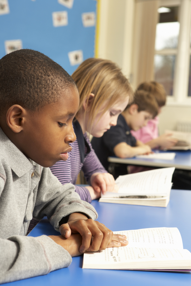 Row of multi-ethnic students reading books aloud in class.  