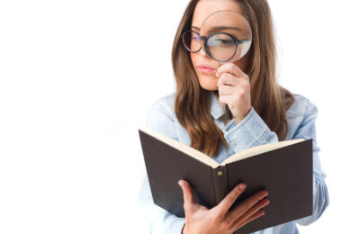 Image shows teacher in blue shirt using a magnifying glass and holding a book.