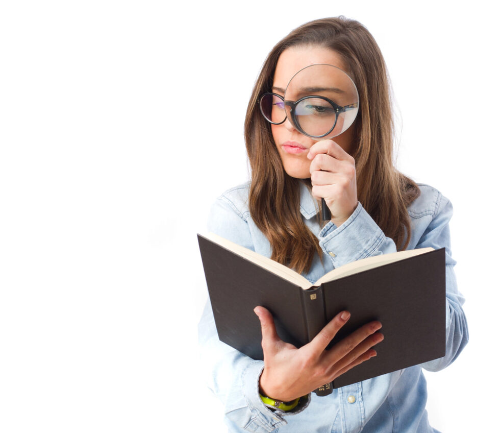 Image shows teacher in blue shirt using a magnifying glass and holding a book.