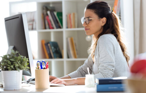 Image shows young female teacher planning lessons at computer.