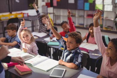 Image shows diverse schoolchildren raising hands indicating high student engagement.