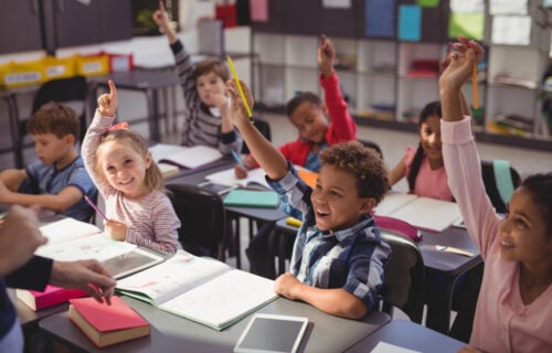 Image shows diverse schoolchildren raising hands indicating high student engagement.
