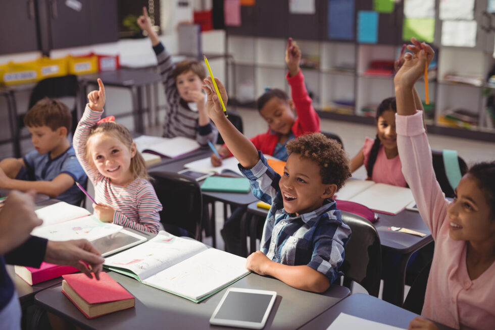 Image shows diverse schoolchildren raising hands indicating high student engagement.
