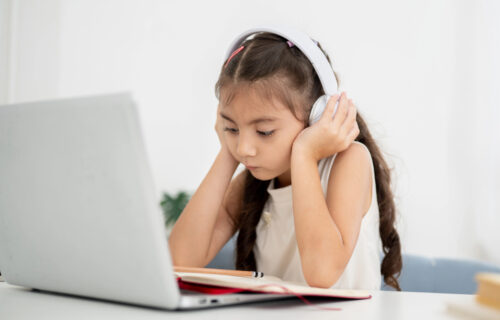 Little girl concentrating on reading in classroom through an online platform using AI.