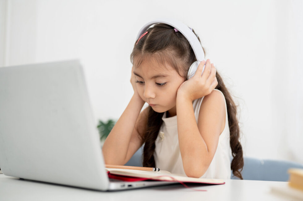 Little girl concentrating on reading in classroom through an online platform using AI.