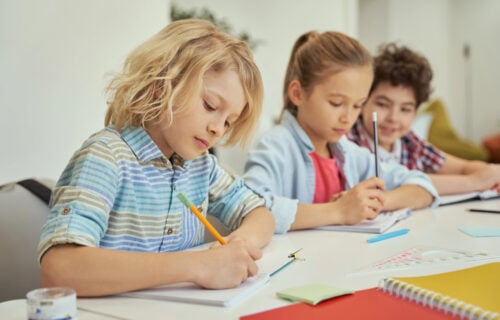 Schoolchildren wearing blue writing sentences with pencils in notebooks at school.